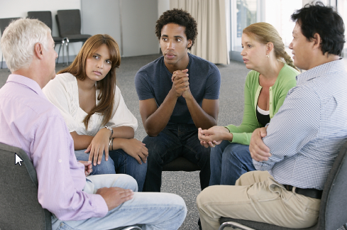 An image of 5 people sitting in a circle- depicting a support group setting. 